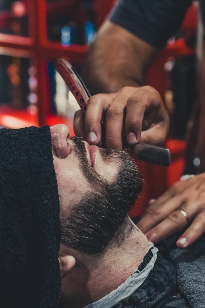 Peluqueria Xerica en Carlet. A barber skillfully shaves a mans beard using a straight razor at a barbershop.