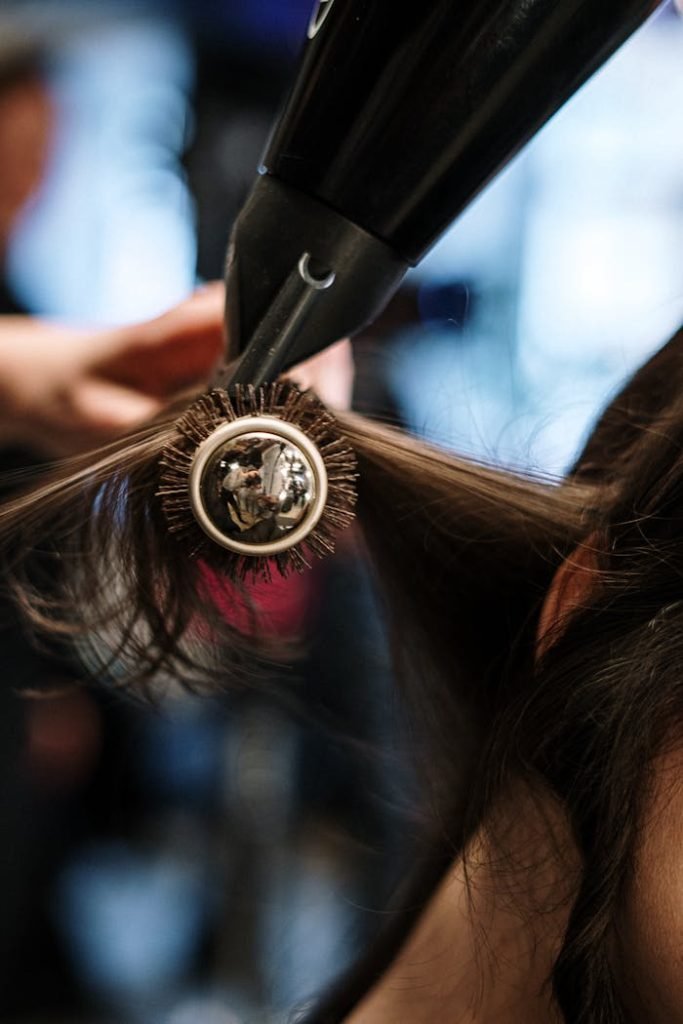 Servicios de Peluqueria. Close-up of a hairstylist styling hair with a brush and dryer in a salon setting.